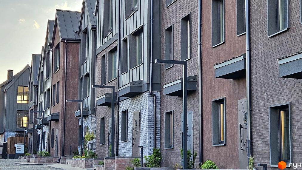 Зовнішній вигляд таунхаусів New Smart 17 з цегляним фасадом та металевим дахом. Навколо будівель облаштована прибудинкова територія з освітленням та зеленими насадженнями.