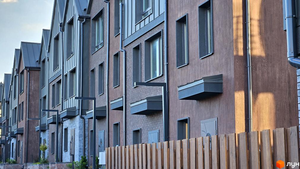 Фасад житлового комплексу New Smart 17 з цегляним оздобленням та великими вікнами. Поруч дерев'яний паркан та зелені насадження.