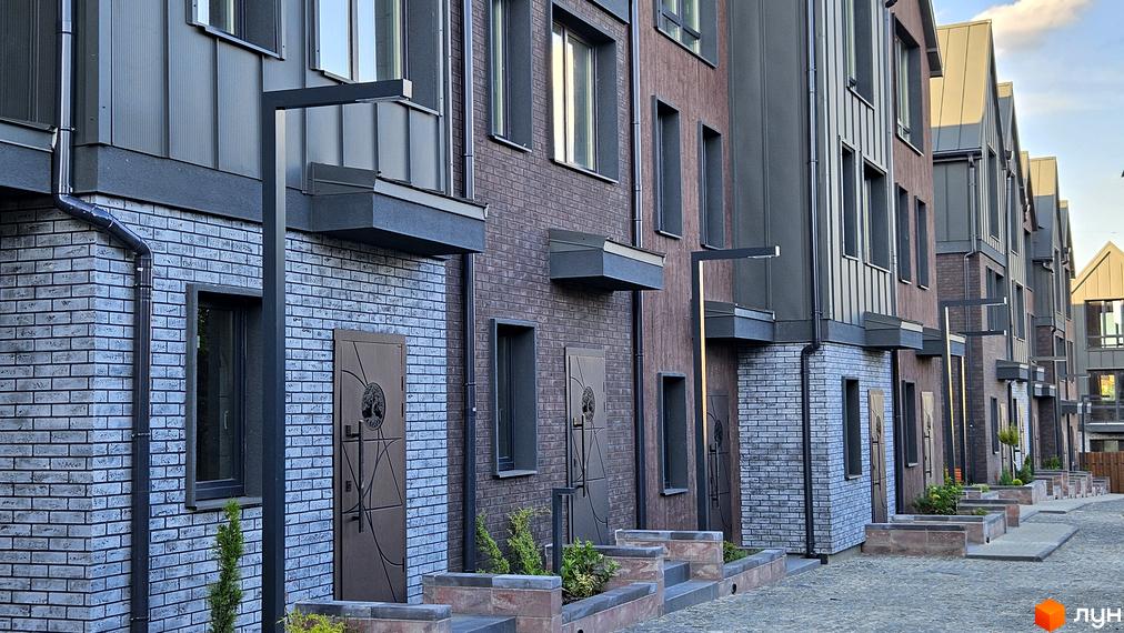 Зовнішній вигляд таунхаусів New Smart 17 з цегляним фасадом та сучасними дверима. Прибудинкова територія з бруківкою та зеленими насадженнями.