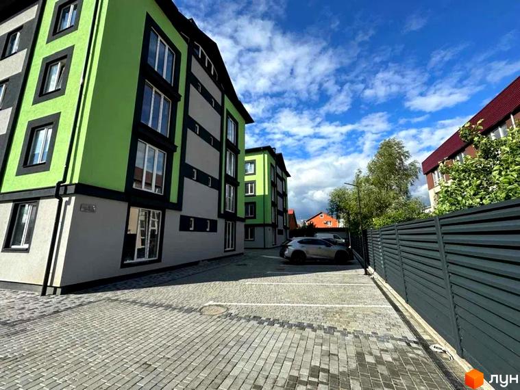 Зовнішній вигляд новобудови на вулиці Інститутська, 67а, з яскравим зеленим фасадом та сірими елементами. Прибудинкова територія облаштована парковкою з бруківки.