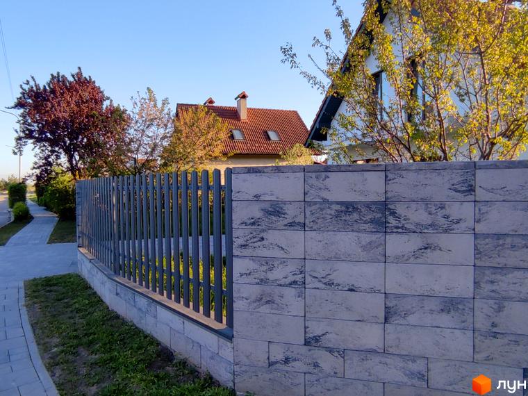 Котеджне містечко КМ Ivankovo з сірим парканом та бруківкою. Навколо будинку зелені дерева та кущі.