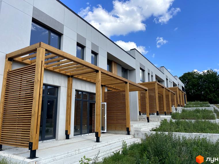 Таунхауси FIRST - сучасні таунхауси з дерев'яними перголами та сходами, що ведуть до зеленої прибудинкової території.