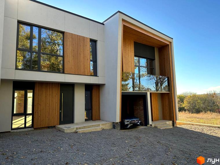 Таунхауси FIRST - двоповерховий будинок з дерев'яними елементами, великими вікнами та прибудинковою територією з гравієм.