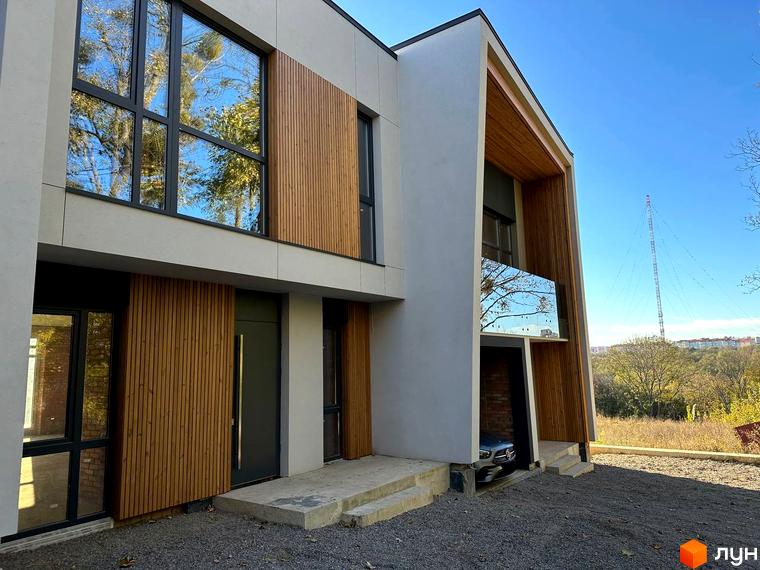 Таунхауси FIRST - двоповерховий будинок з дерев'яними та світлими фасадами, великими вікнами та прибудинковою територією з гравієм та деревами.