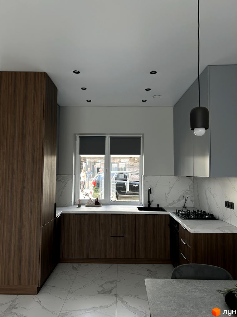 Сучасна кухня з дерев'яними фасадами та мармуровою стільницею. Вікно з видом на вулицю з автомобілями та людьми.