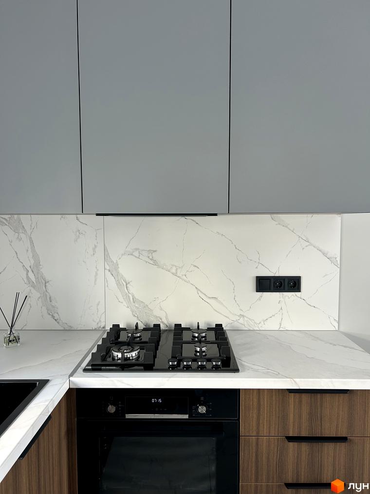 Сучасна кухня з мармуровою стільницею та вбудованою технікою. Кухонні шафи світло-сірого кольору, стільниця з білого мармуру з сірими прожилками.