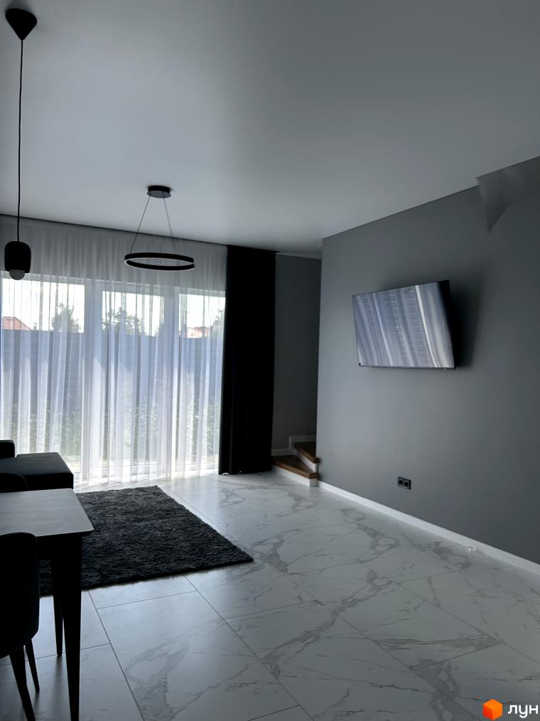 Вітальня в Peremohy Homes з великими вікнами, що виходять на зелену зону. Сучасний дизайн інтер'єру з сірими тонами та мінімалістичними меблями.