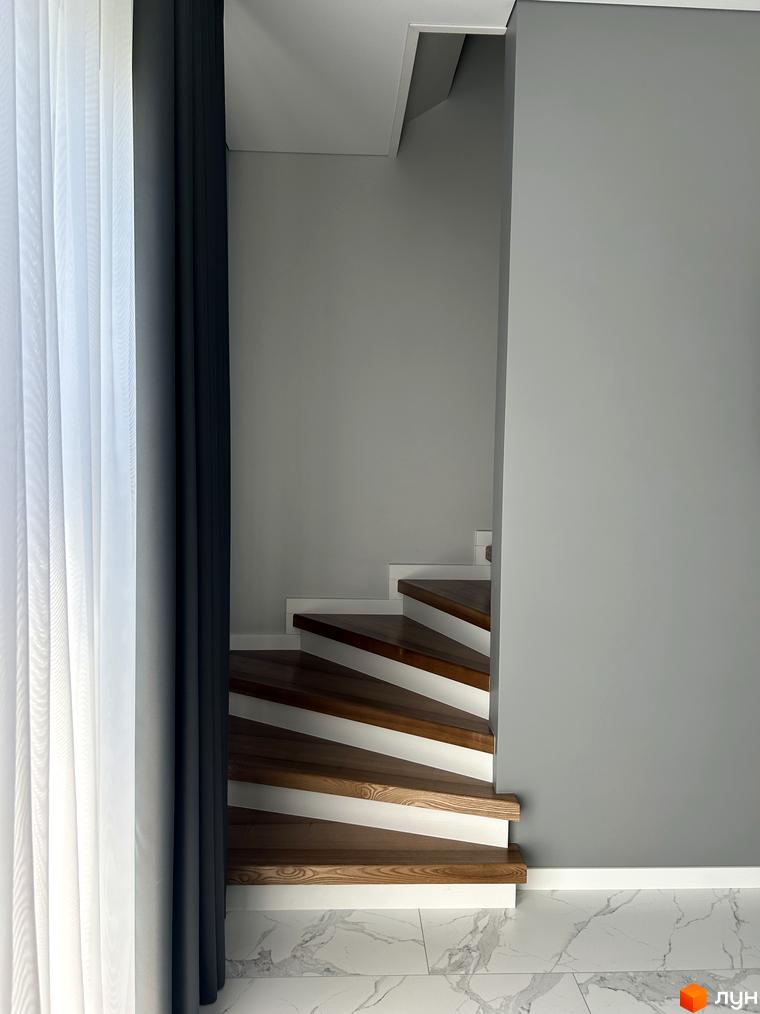 Сходи в Peremohy Homes з дерев'яними ступенями та білими підсвічуваннями. Сучасний дизайн інтер'єру новобудови.