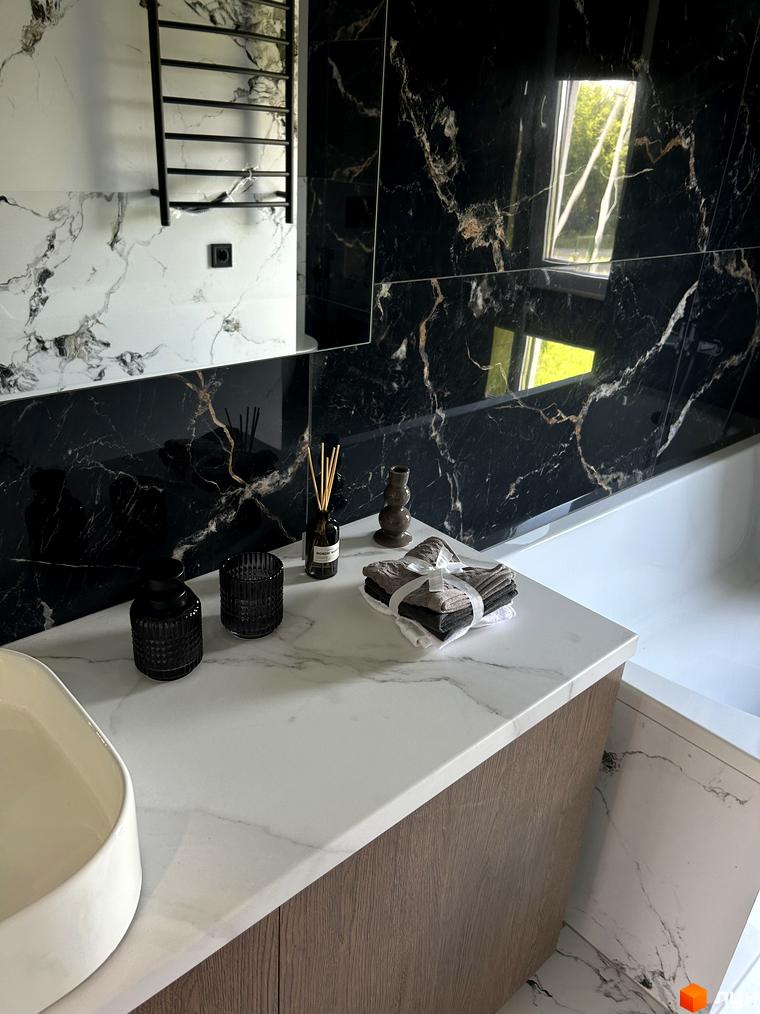 Сучасний дизайн ванної кімнати з мармуровим оздобленням та елементами чорного кольору. На стільниці розташовані аксесуари для ванної кімнати, включаючи аромадифузор та рушники.