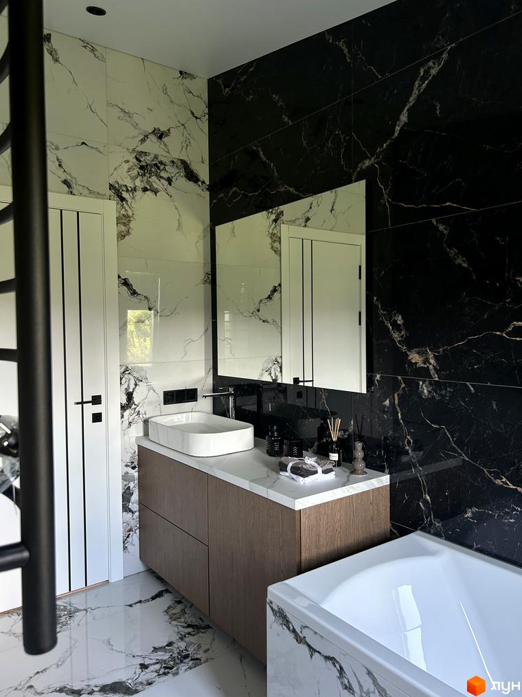 Дизайн ванної кімнати в Peremohy Homes з мармуровим оздобленням стін та підлоги, білою раковиною та дерев'яною тумбою. Ванна кімната виглядає просторою та сучасною.