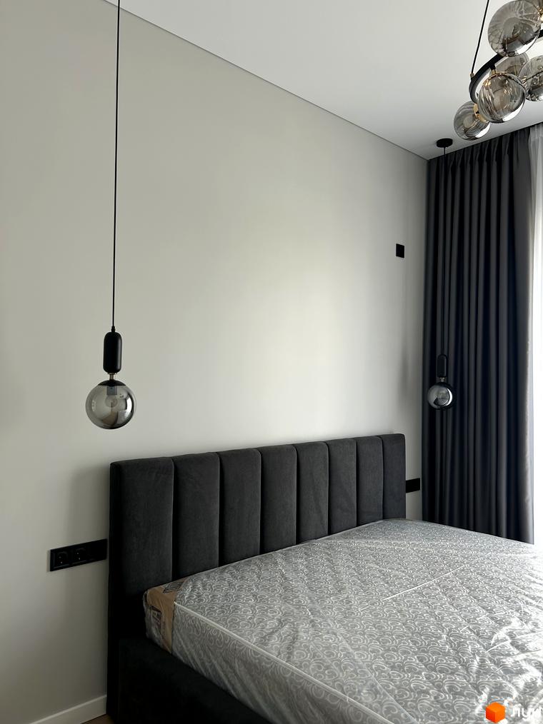 Інтер'єр спальні в Peremohy Homes з двоспальним ліжком та приліжковими світильниками. Сучасний дизайн кімнати з сірими шторами та білими стінами.