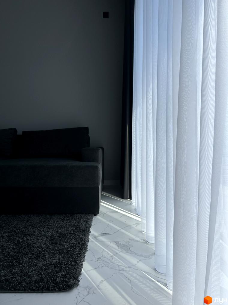 Інтер'єр таунхаусу Peremohy Homes з диваном та килимом біля вікна з білими шторами, що пропускають сонячне світло. Просувайте сайт новобудов.