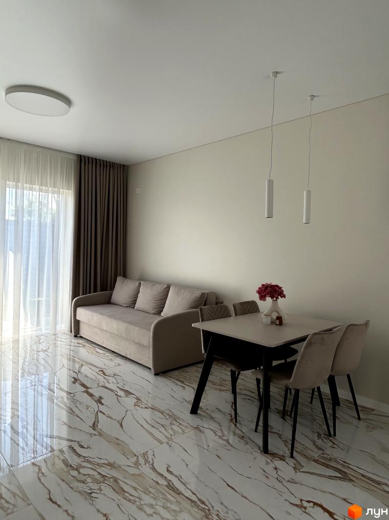 Світла вітальня з диваном та обіднім столом у Peremohy Homes. Великі вікна забезпечують багато природного світла, підкреслюючи мармурову підлогу.