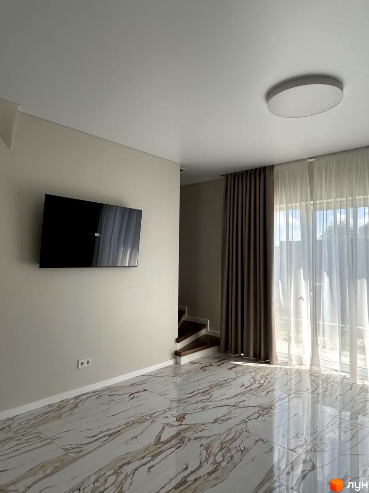 Інтер'єр вітальні в таунхаусах Peremohy Homes з телевізором на стіні та великими вікнами з шторами.