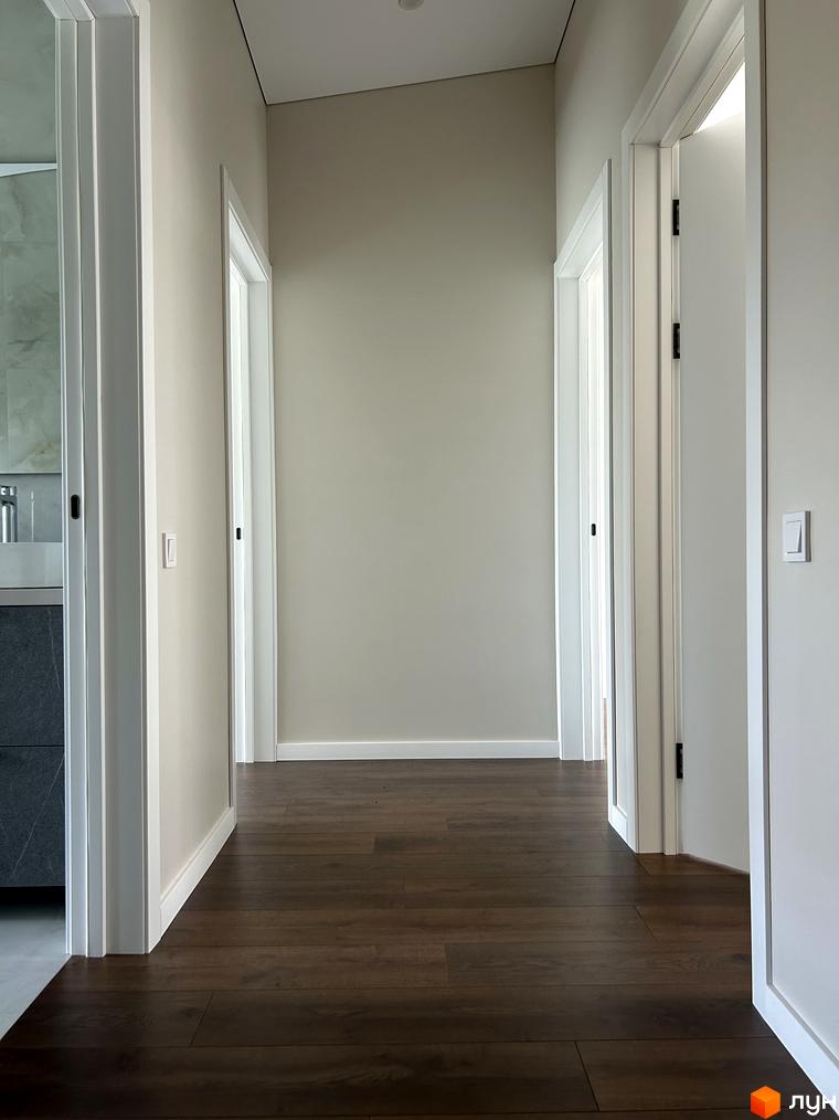 Сучасний коридор з дерев'яною підлогою та білими дверима в житловому комплексі Peremohy Homes. Відкриті двері ведуть до світлих кімнат.