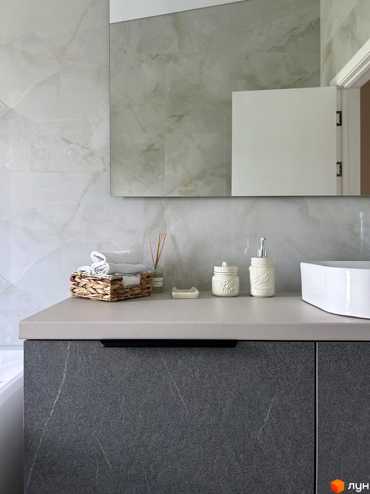 Сучасний дизайн ванної кімнати з мармуровою плиткою та сірою тумбою під раковину. На стільниці розташовані аксесуари для ванної кімнати.