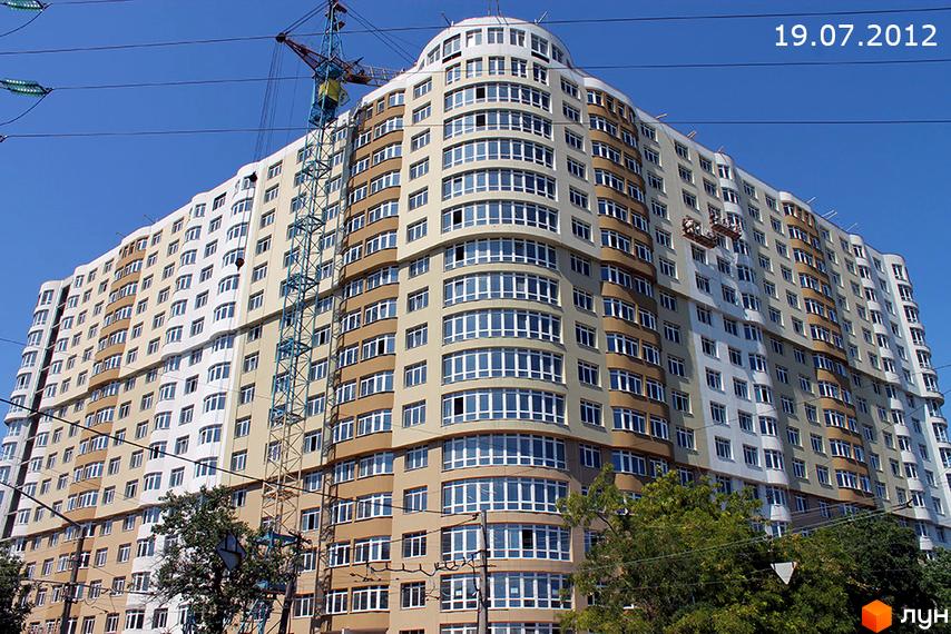 Житловий комплекс на вул. Бреуса, 63, з фасадом, оздобленим вікнами. На передньому плані зелена прибудинкова територія.