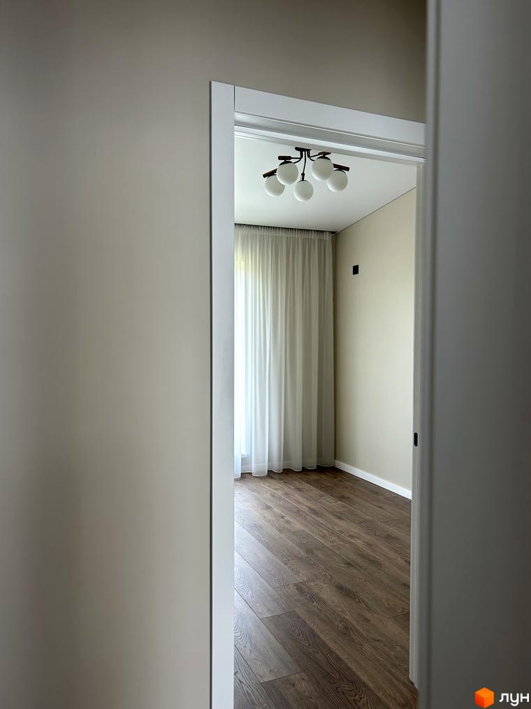 Огляд інтер'єру таунхаусів Peremohy Homes з дерев'яною підлогою та світлими стінами. Вікно з білими шторами пропускає природне світло.