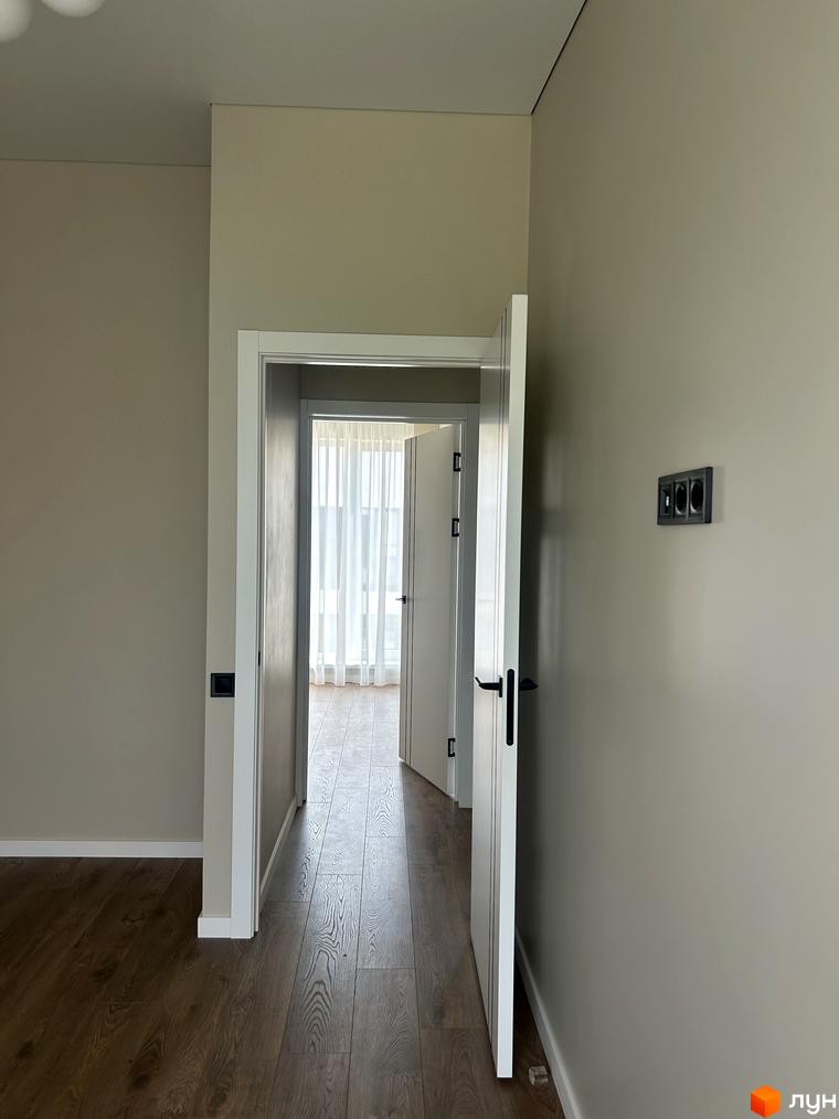 Інтер'єр таунхаусу Peremohy Homes з дерев'яною підлогою та дверима. Відкритий прохід до кімнати з білими шторами.