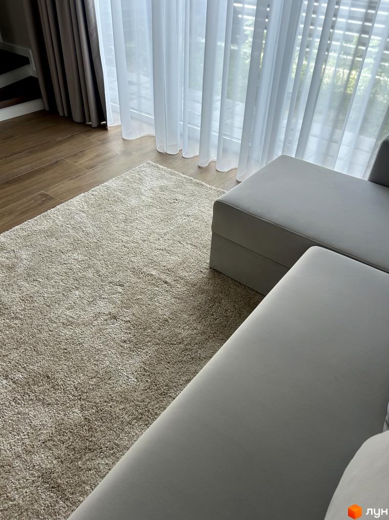 Світлий килим та сірий диван біля вікна з білими шторами в Peremohy Homes. Затишна вітальня з дерев'яною підлогою.