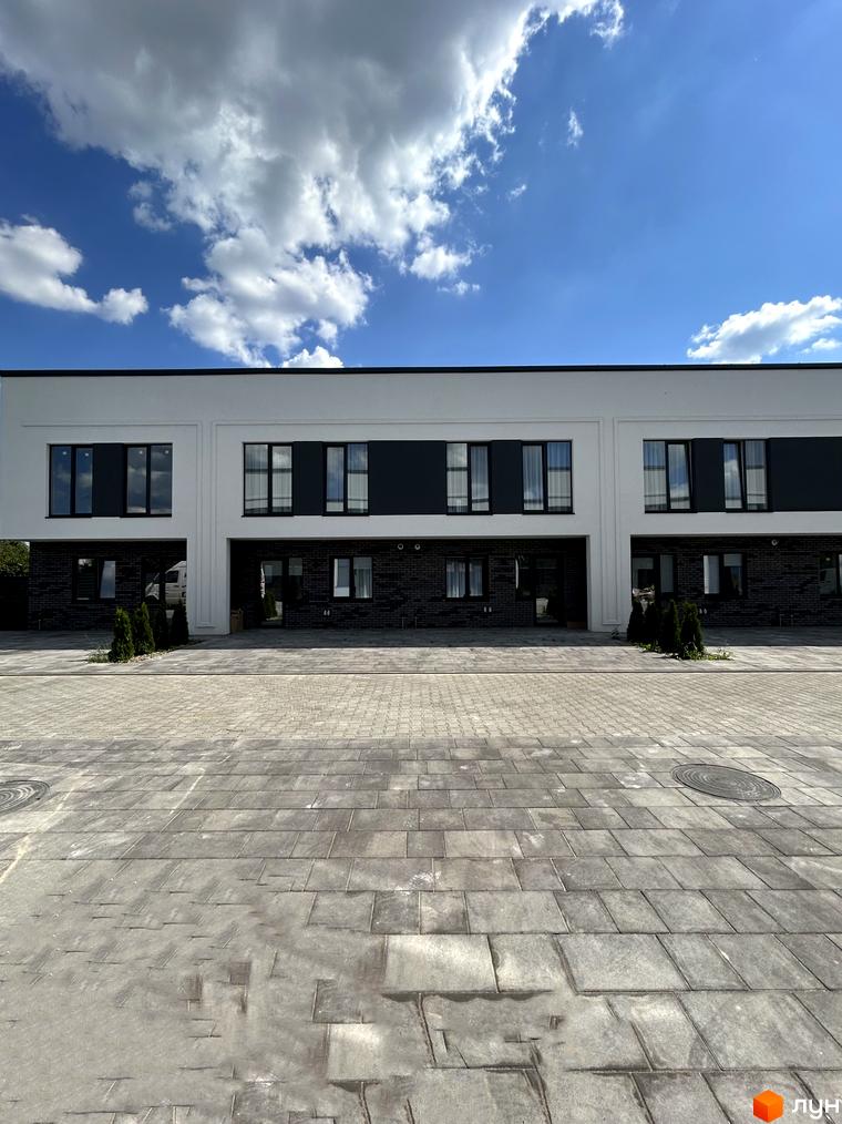 Таунхауси Peremohy Homes - двоповерхові будинки з білою та темною обробкою фасаду, великими вікнами та бруківкою перед будинками.