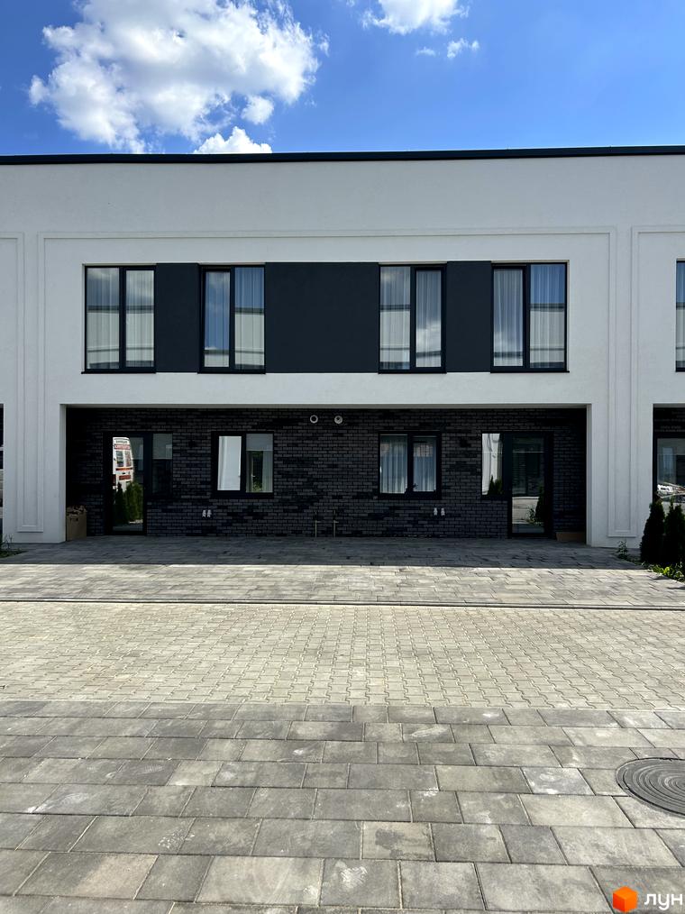 Таунхауси Peremohy Homes з цегляним фасадом та великими вікнами. Перед будинками вимощена сіра бруківка.