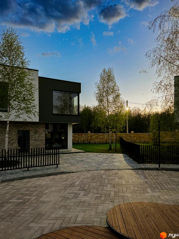 Котеджне містечко Barcelona: двоповерховий будинок з цегляним цоколем та великими вікнами, огороджена територія з бруківкою та деревами.