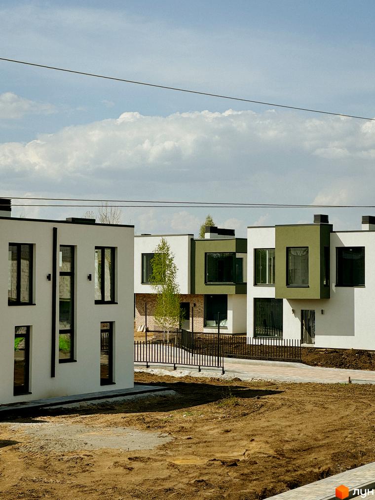 Котеджне містечко Barcelona: білі та зелені будинки з великими вікнами, огороджена територія з парканом, доріжки та ділянка з землею.