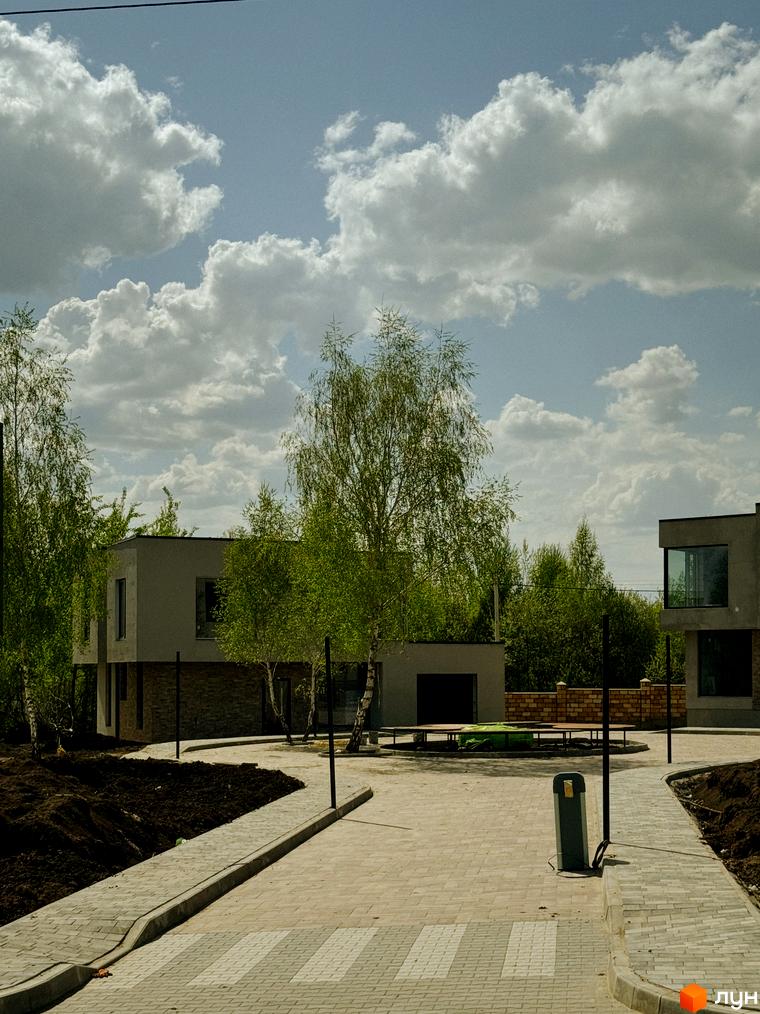 Котеджне містечко Barcelona: сірі будинки з великими вікнами та зелена територія з деревами. Прибудинкова територія з бруківкою та газоном.