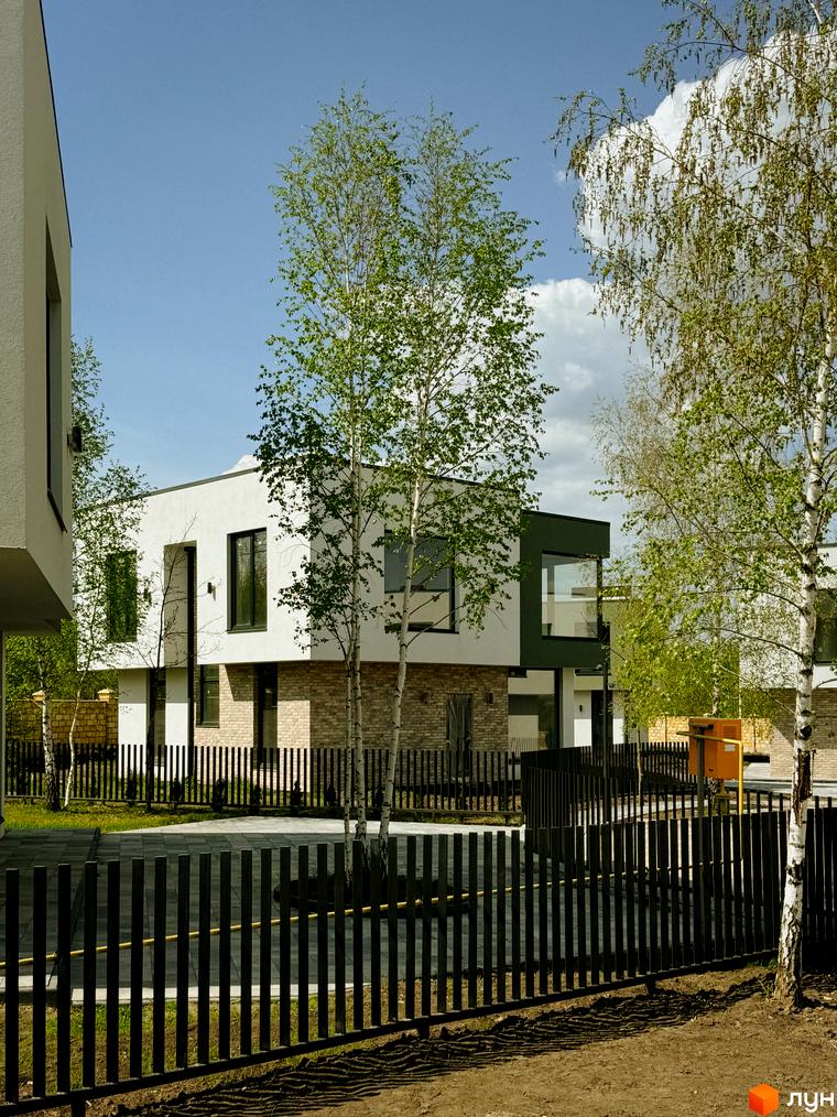 Котеджне містечко Barcelona: двоповерхові будинки з білою та темно-зеленою обробкою, великими вікнами та цегляною основою, оточені деревами та огороджені чорним парканом.