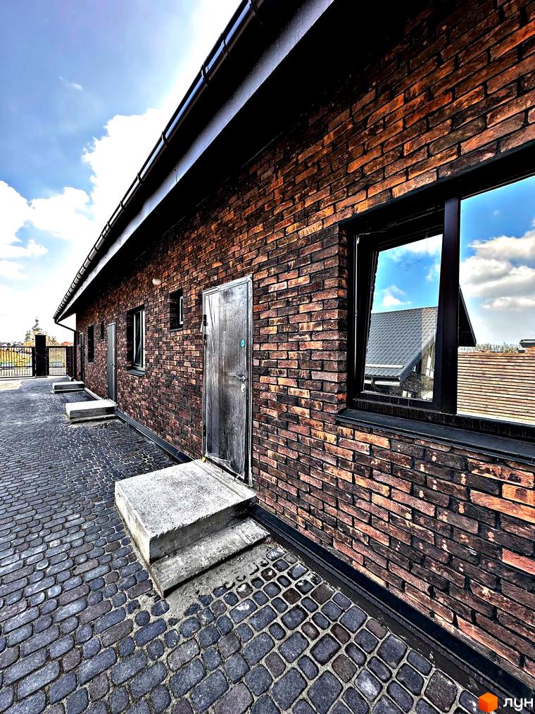 Фасад таунхауса з цегляною кладкою та бруківкою на території. Одноповерховий Київ - Малехів - це житловий комплекс з унікальною архітектурою.