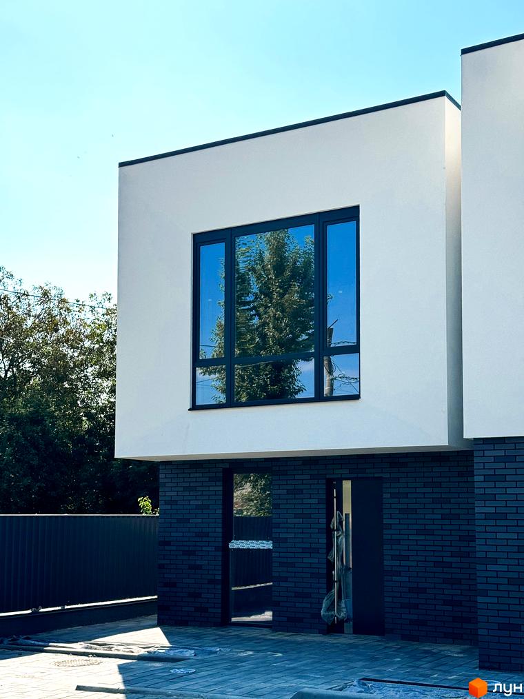 Сучасний житловий комплекс на вул. Троянівська, 21а, з білими фасадами та великими вікнами. Прибудинкова територія з плиткою та парканом.