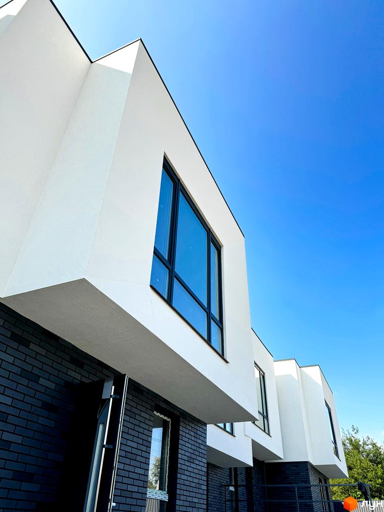 Сучасний житловий комплекс на вул. Троянівська, 21а. Фасад новобудови оздоблений білою штукатуркою та темною цеглою, великі вікна.