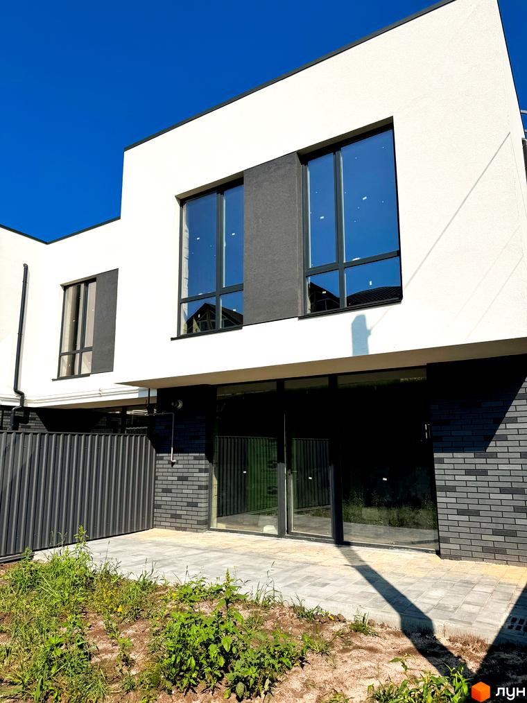 Сучасний житловий комплекс на вул. Троянівська, 21а, з білою штукатуркою та темними вставками, великими вікнами та вимощеною прибудинковою територією.