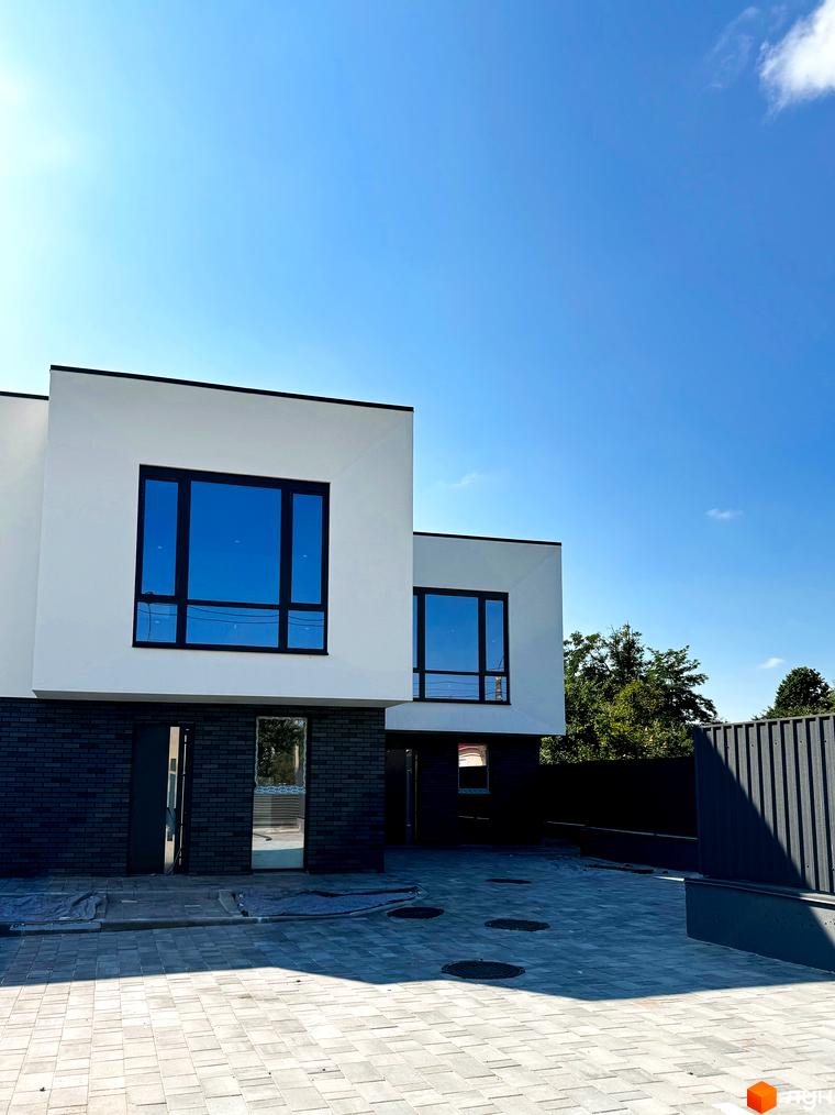 Зовнішній вигляд новобудови на вул. Троянівська, 21а з великими вікнами та цегляним цоколем, на прибудинковій території викладена бруківка.