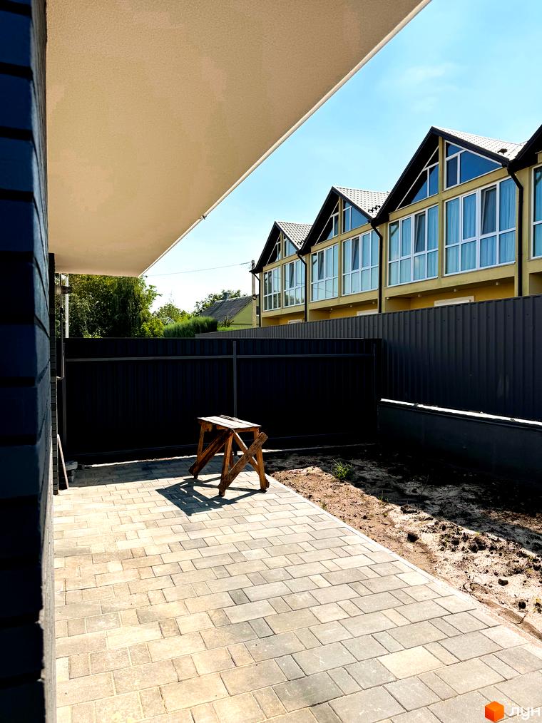 Зовнішній вигляд новобудови на вул. Троянівська, 21а з патіо та парканом. Навколо будинку облаштована прибудинкова територія.