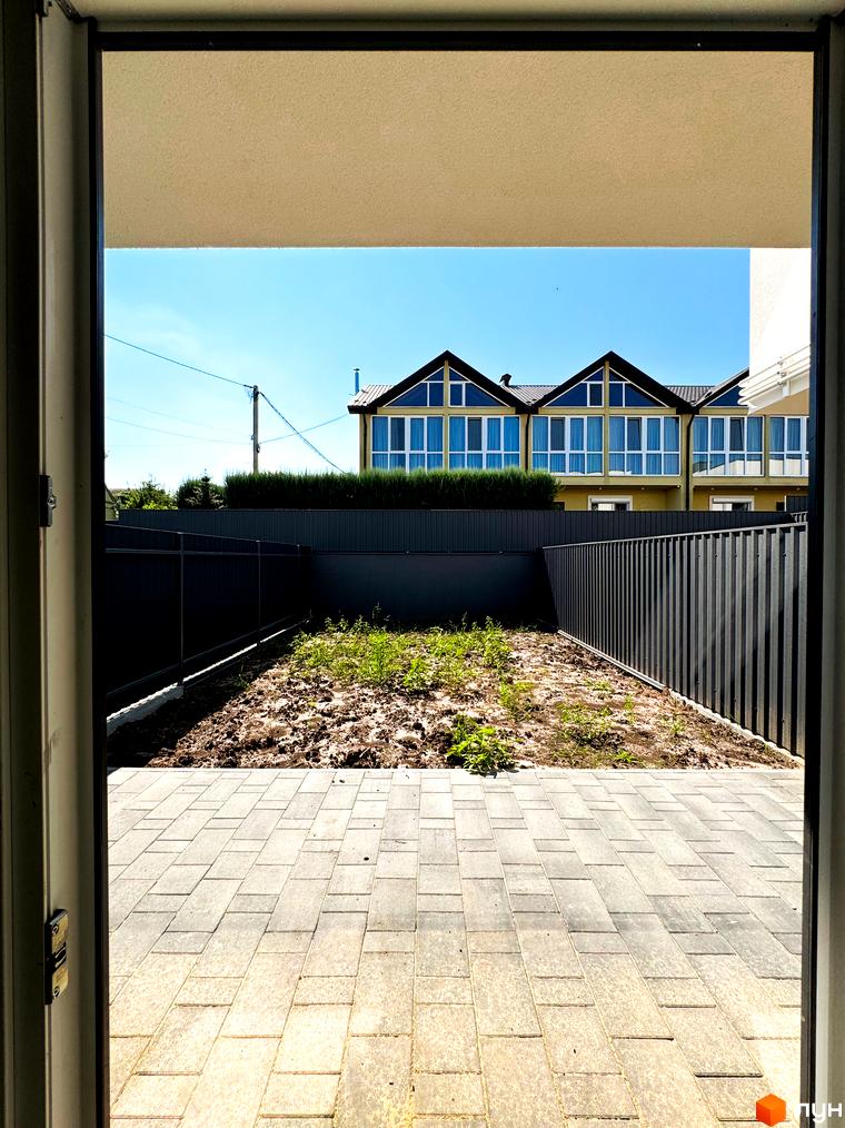 Зовнішній вигляд новобудови на вул. Троянівська, 21а, з патіо та огорожею. Навколо зелені насадження та паркан.