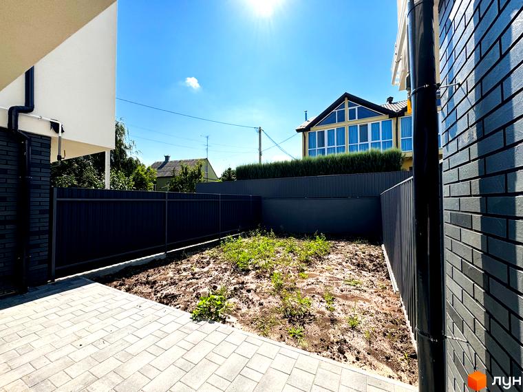 Зовнішній вигляд будинку з великими вікнами та прибудинкова територія з бруківкою та парканом на вулиці Троянівська, 21а. Новобудова з огородженою ділянкою.