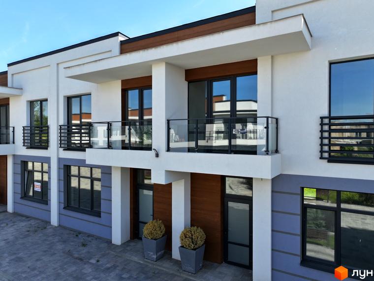 Фасад котеджного містечка City Villa Club з великими вікнами та скляними балконами. Прибудинкова територія з бруківкою та зеленими насадженнями.