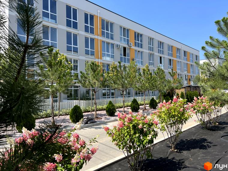 Житловий комплекс Sanville Park з елегантним фасадом та доглянутою прибудинковою територією з квітучими кущами та деревами.