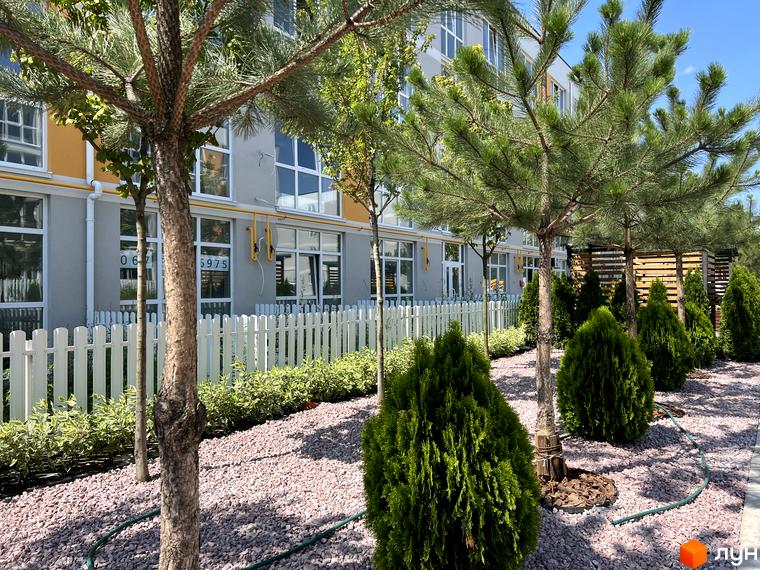 Житловий комплекс Sanville Park: фасади будівель з великими вікнами, огороджені білою парканом, та доглянута прибудинкова територія з деревами та кущами.