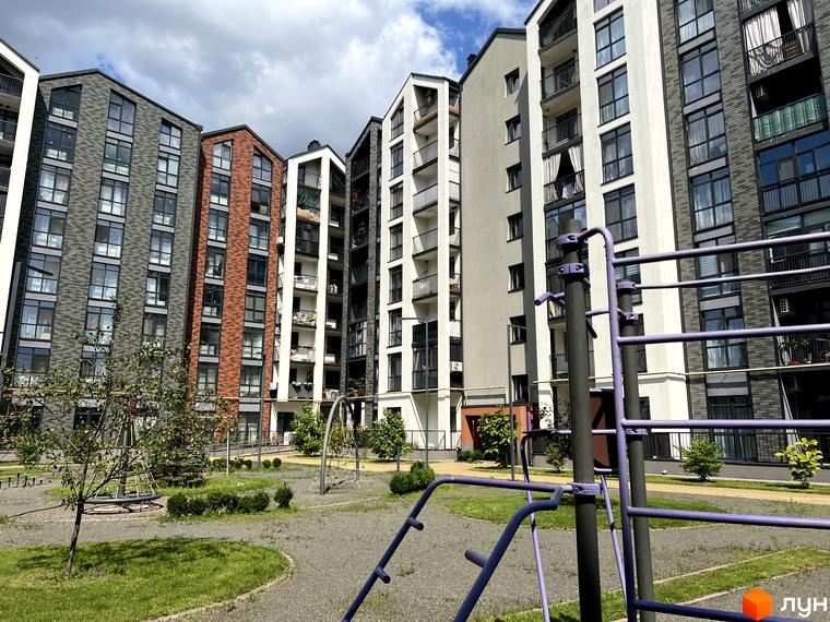 Житловий комплекс Scandia: фасади будинків з цегли та штукатурки, вікна з чорними рамами, дитячий майданчик та зелень на прибудинковій території.