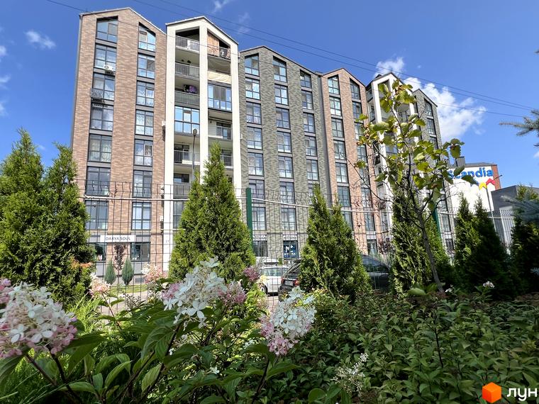 Житловий комплекс Scandia з цегляним фасадом та балконами, оточений зеленими деревами та квітами.