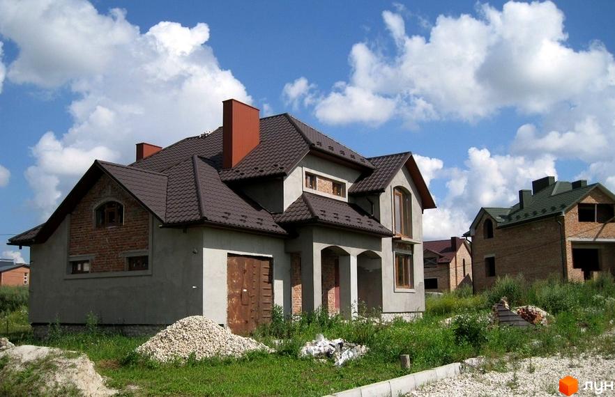 Котеджне містечко Кленовий гай: будівництво будинків з коричневим дахом та цегляними елементами. Навколо зелена територія з будівельними матеріалами.