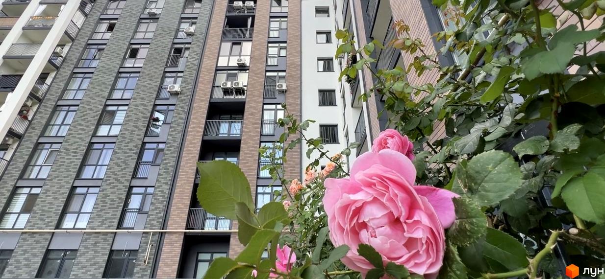 Зовнішній вигляд багатоповерхового будинку ЖК Scandia з цегляним фасадом та кондиціонерами на балконах. Поруч квітуча троянда.