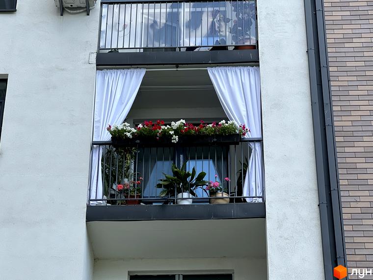 Житловий комплекс Scandia: балкон з квітами та білими шторами на фасаді будинку. Зовнішній вигляд новобудови.