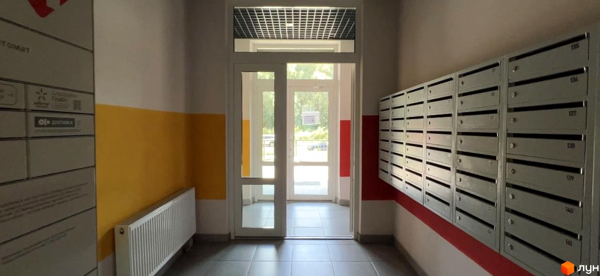 Під'їзд житлового комплексу Scandia з поштовими скриньками та дверима назовні. Зовнішній вигляд будинку з жовтою та червоною смугами на стінах.