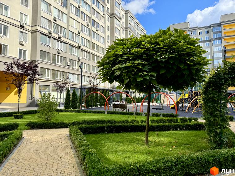 Житловий комплекс Millennium State з фасадами сірого кольору та жовтими акцентами, з дитячим майданчиком та зеленими насадженнями.