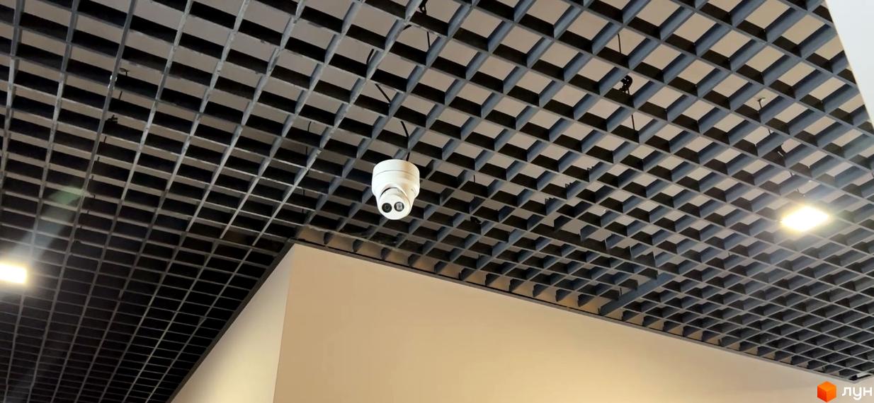 Камера відеоспостереження на сітчастій стелі житлового комплексу Scandia. Навколо видно квадратні секції стелі та освітлення.