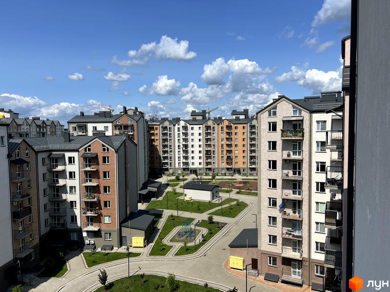 Житловий комплекс Scandia: багатоповерхові будинки з цегляним та білим фасадом, балконами, сірими дахами. На прибудинковій території зелені зони, дитячі майданчики та дороги.